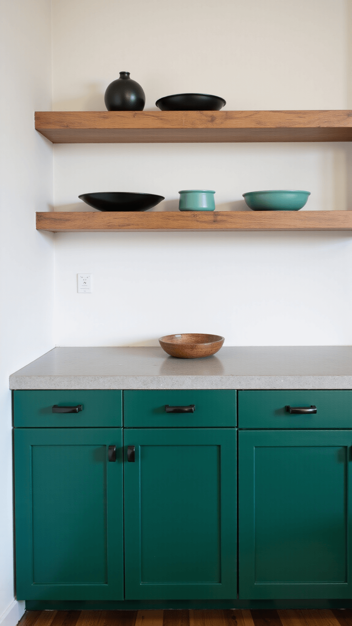 Mid-sized 15x12ft kitchen with emerald green cabinets, concrete countertops, and open shelves displaying ceramics against a white wall, highlighted by soft box lighting during golden hour