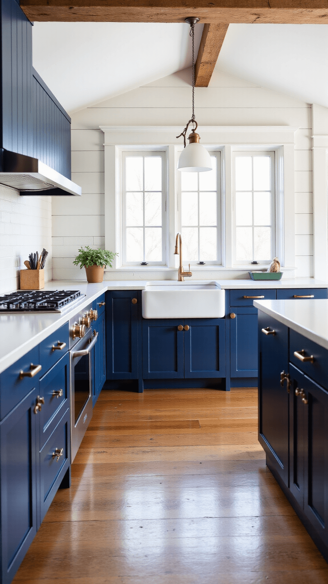 Mid-morning in a farmhouse-style kitchen with navy blue cabinets, cream quartz countertops, brass hardware, farmhouse sink, gold faucet, white shiplap walls, wide-plank floors, and cathedral ceiling with exposed beams, illuminated by natural light from mullioned windows.
