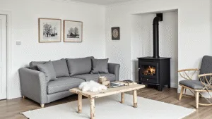 "Nordic cabin interior featuring white walls, grey linen sofa, black wood stove, birch furniture, sheepskin throws, with morning light highlighting the minimal styling on a clean background"